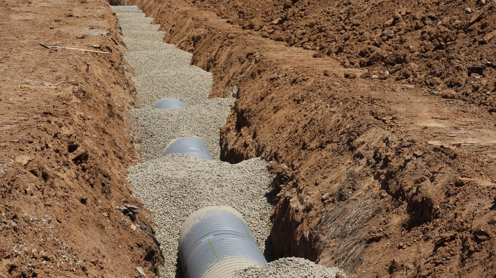 new pipe bedded on gravel in a red clay trench, the way a sewer line replacement is supported so that it keeps its fall