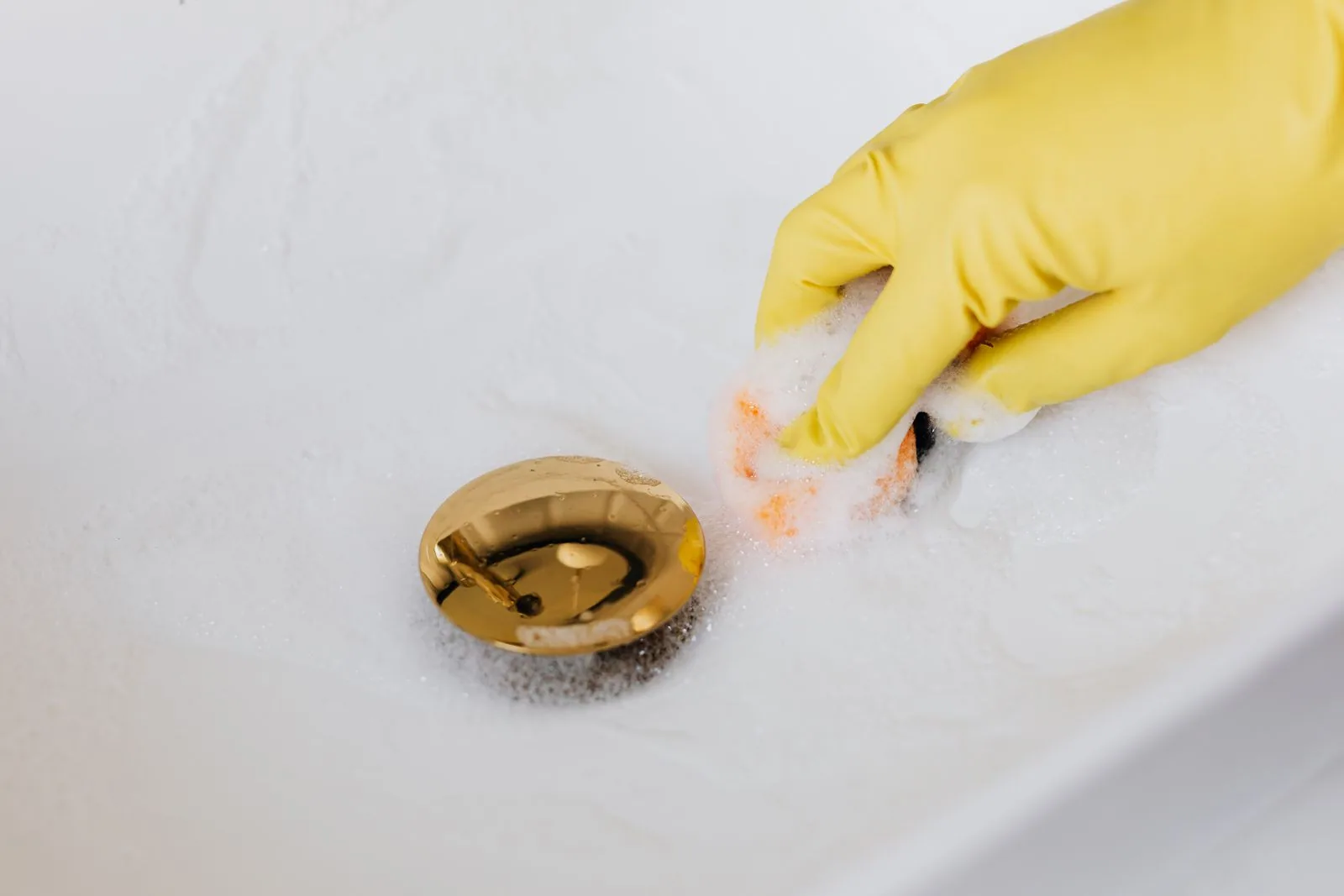 gloved hand cleaning around the pop-up stopper of a white bathroom sink drain